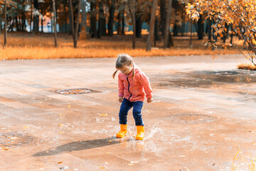 child jumping and playing in a puddle after rain on an autumn sunny day