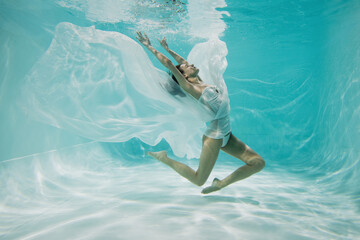 graceful young woman in white dress diving in swimming pool