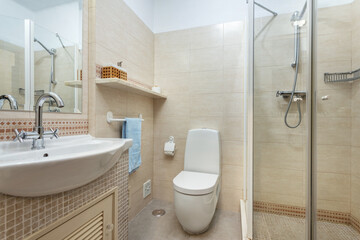 Modern tiled gray bathroom of a resort, with a sink facing a toilet and a shower at the end of the room.