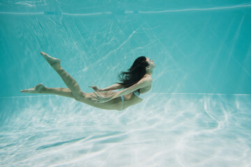 graceful young woman in white swimsuit diving in swimming pool