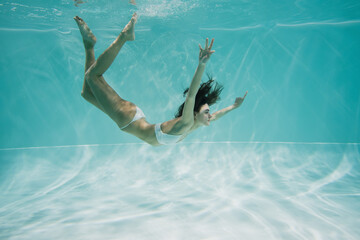 graceful and brunette woman in white swimwear swimming in pool