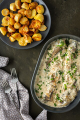 Stewed hake in a creamy sauce with baked potatoes, delicious hearty lunch, top view