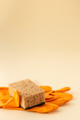 Brown dishwashing sponge and orange rubber gloves on neutral beige background, cleaning concept