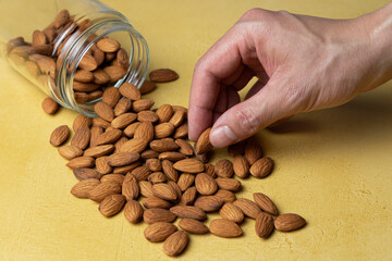 Hand picking up a peeled almond from a pile on a yellow table