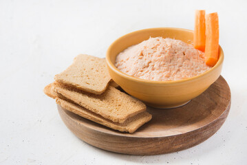 Smoked salmon and soft cheese spread pate with brown bread and carrot on white background.