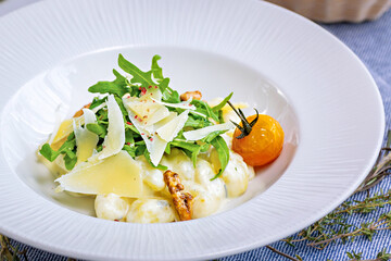Salad with slices of cheese, tomatoes, potatoes and walnuts on a large white plate in a restaurant. Restaurant menu