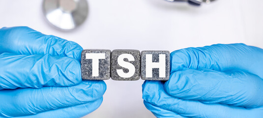 TSH Thyroid stimulating hormone - word from stone blocks with letters holding by a doctor's hands in medical protective gloves