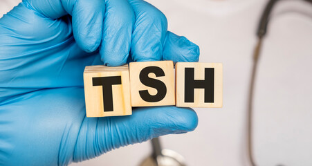 TSH Thyroid stimulating hormone - word from wooden blocks with letters holding by a doctor's hands in medical protective gloves. Medical concept.