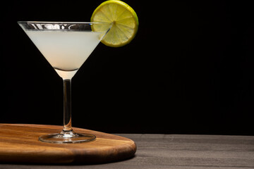 Close-up of cocktail glass with lime slice on dark wooden table and table, black background, horizontal, with copy space