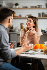 Beautiful young girl enjoying in breakfast with her boyfriend. Loving couple drinking coffee in the kitchen..