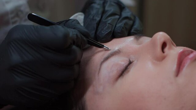 close up of female at beautician on correction eyebrow procedure with tweezers