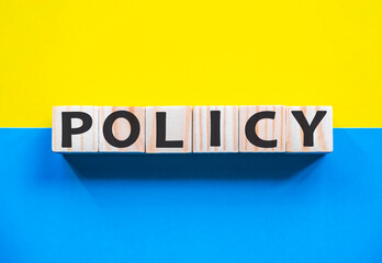 Word POLICY on wooden cubes with word on beautiful yellow and blue background. Business, media marketing concept.