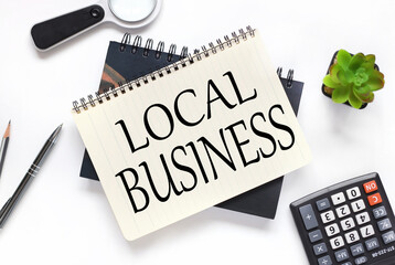 local business. an open notebook lies on a closed notebook near a calculator and a magnifying glass on a white workspace.