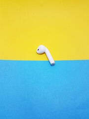 white airpod plced on yellow and sky bckground