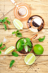Moscow mule alcoholic cocktail in copper mug with lime, ginger beer, vodka and mint. Wooden bar counter, bartender work tools, top view