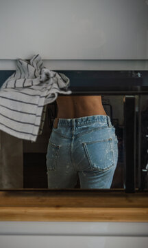 Mujer joven con pantal&oacute;n vaquero reflejada en la puerta de espejo de un microondas en la cocina
