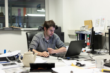 Angestellter sitzt abends allein im Büro vor Laptop und arbeitet