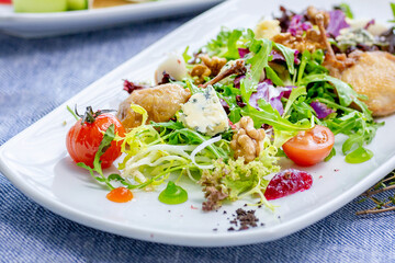 Salad with chicken, dor blue cheese, walnuts, tomato, arugula on a white platter. Restaurant menu. Close-up