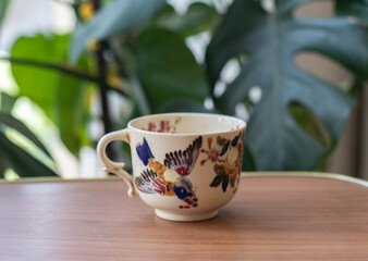 Vintage fayence coffee cup with bird pattern on a wooden table with plants in the background