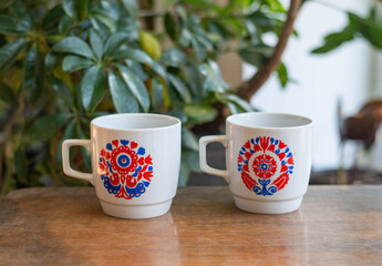 Mid-century modern porcelain cups with red and blue flower pattern on a wooden table with plants in the background