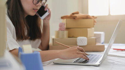 Beautiful young asian business owner working with computer and tablet standing in workshop.Responding on business e-mail,writing the order of product customer orders.