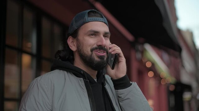 Young, modern handsome man talking on the phone on the street of a small town on a sunny spring day.