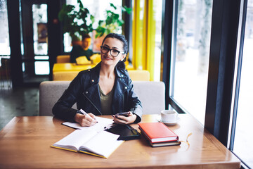 Smiling woman writing notes in notepad in cafeteria