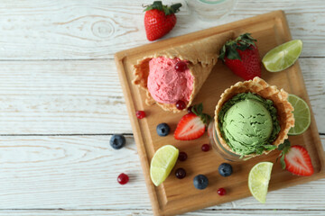 Cones with ice cream and ingredients on white wooden background