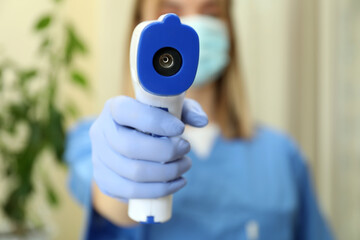 Female doctor holds thermometer gun, close up and front view