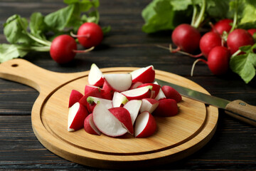 Cutting board with chopped radish on wooden background