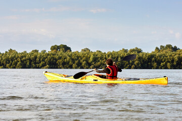 Teenage boy paddling in yellow kayak at the river at summer time