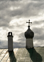 Roof with a dome and a cross. Gray clouds and sun. The shadows from the dome fall on the roof. 