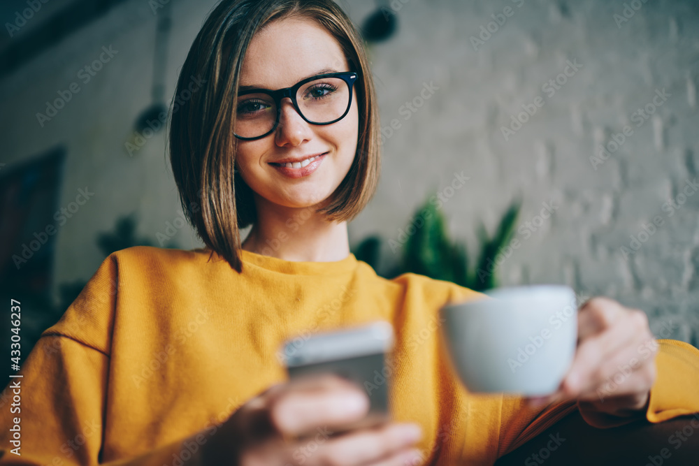 Aufkleber portrait of happy caucaisan user with modern cellphone device and tea cup in hands smiling at camera