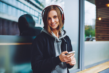 Portrait of pretty Caucaisan tourist in modern earphones connecting to bluetooth application on...