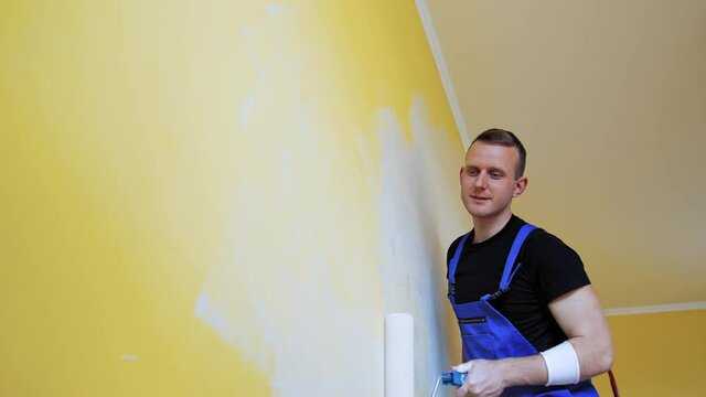 Attractive painter doing new interior of wall. Cheerful man working with paintings.