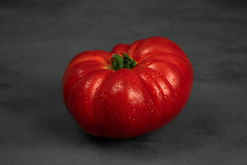 Single big tomato on dark grey background.