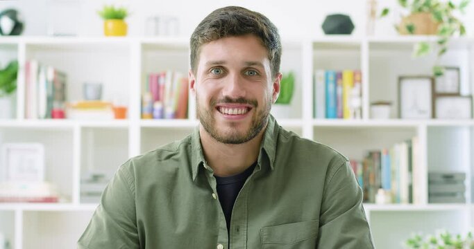 Slow motion of focused confident handsome young adult entrepreneur or posing at home. Smart bearded millennial professional businessman looking at camera and smiling.