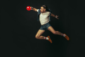 Young caucasian man playing tennis isolated on black studio background in retro style, action and...