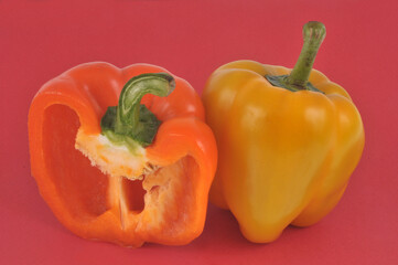 Poivron jaune entier et poivron orange coupé en gros plan sur fond rouge