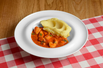 Mashed potato with gravy poured over. Served in a white plate over red plaid table cloth.