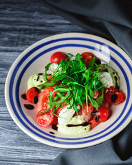 Salad with tomatoes and mozzarella topped with fresh arugula. Italian cuisine concept. Salad served in a white plate.