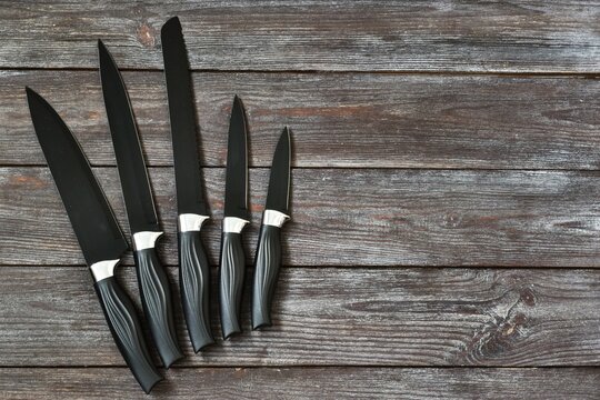 Kitchen black knifes set lies on a wooden background. Flat lay, copy space.