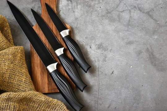 Kitchen black knifes set lies on wooden cutting board on a gray concrete background. Flat lay, copy space.