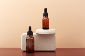Two dark bottles with skin serum or oil for nails with beige geometric props on brown table against beige background with copy space. Concept of skin care or manicure