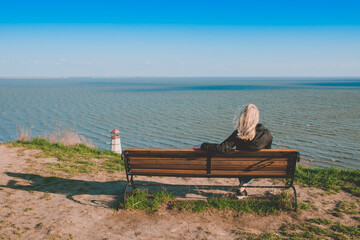 A man sits on a bench with his back and looks at the sea in the distance. A man looks at the sea