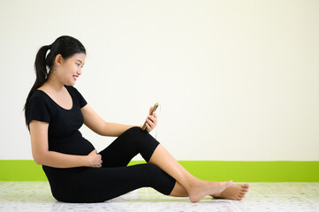 Fototapeta premium A pregnant woman in black happily photographed herself in a white room.