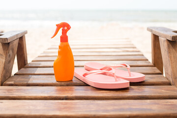 Pink vibrant beach flip flops with sunscreen protection body cream, sea background. Tropical summer...