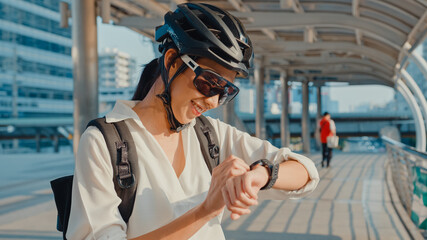 Asian businesswoman with backpack bicycle smiling look smartwatch in city street go to work at...