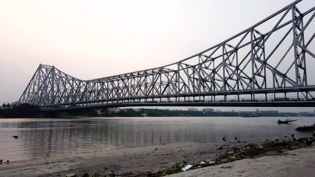 KOLKATA, INDIA - May 02, 2021: Wooden fishing boats on river Ganges with view of Howrah Bridge a cable stayed bridge at Kolkata India at sunset