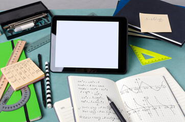 Mathematics practice, exams concept.Closeup of blank screen of tablet, math notes, books, notebooks, rulers, pencils on the desk